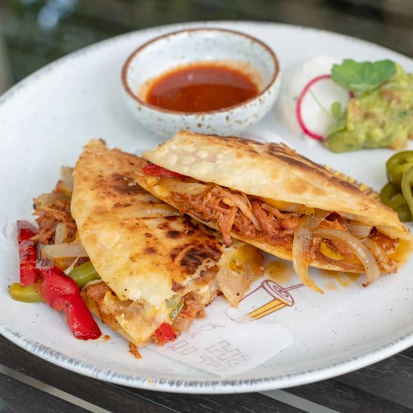 Two quesadillas filled with shredded meat, onions, and peppers, served with salsa, guacamole, and sour cream.