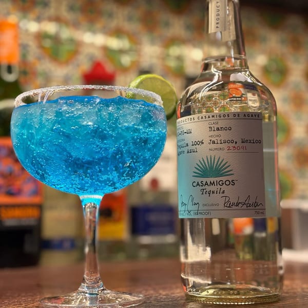 A vibrant blue margarita with a salted rim and lime, next to a bottle of Casamigos Tequila.