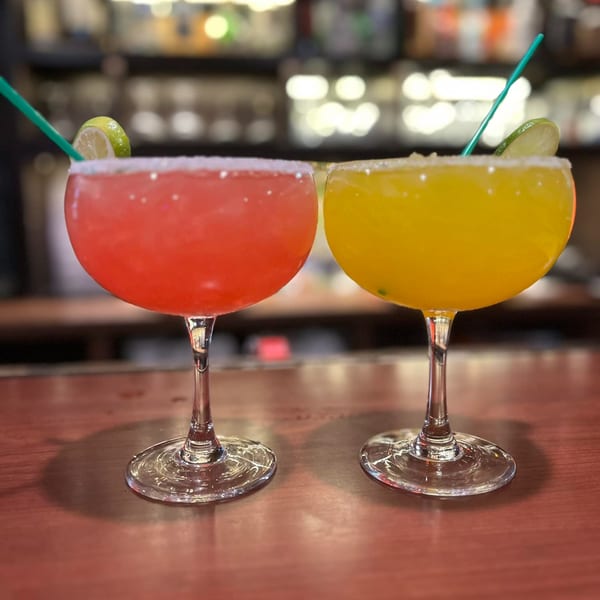 Two vibrant margaritas, one red and one yellow, garnished with lime and salt, on a bar.