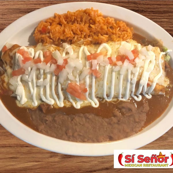 A large burrito covered in sour cream, diced tomatoes, and onions, served with rice and refried beans.