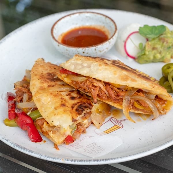 Two Si Senor quesadillas filled with meat, onions, and peppers, served with salsa, guacamole, and sour cream.